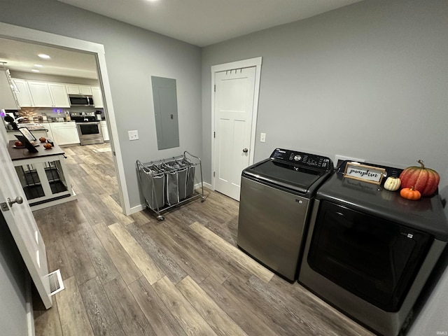 washroom with wood-type flooring, electric panel, and washer and dryer