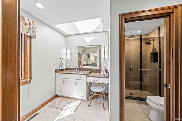 bathroom featuring a shower with shower door, toilet, vanity, and a skylight