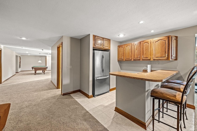 kitchen with billiards, light carpet, stainless steel fridge, a kitchen bar, and a textured ceiling