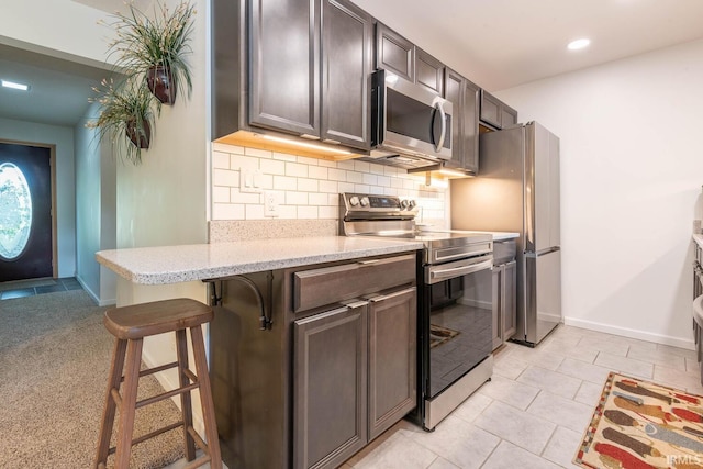 kitchen with light stone counters, a breakfast bar, stainless steel appliances, backsplash, and dark brown cabinetry