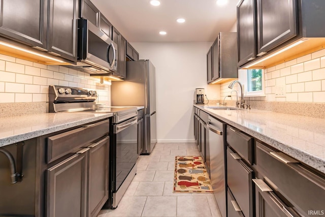 kitchen featuring tasteful backsplash, light stone countertops, stainless steel appliances, a sink, and light tile patterned flooring