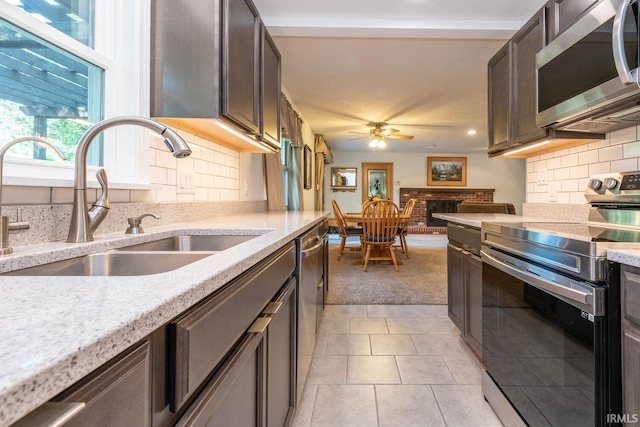 kitchen with ceiling fan, stainless steel appliances, dark brown cabinets, a fireplace, and a sink