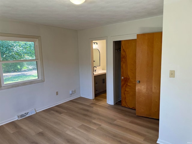 unfurnished bedroom featuring hardwood / wood-style flooring, ensuite bath, sink, a closet, and a textured ceiling