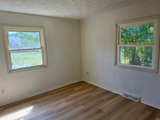 unfurnished room with a textured ceiling, plenty of natural light, and hardwood / wood-style floors