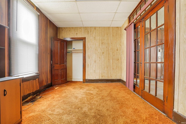 unfurnished bedroom featuring a closet, wooden walls, a paneled ceiling, and carpet floors