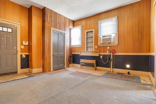 entryway with cooling unit, heating unit, wooden walls, and a textured ceiling