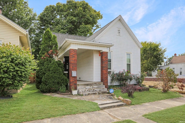 view of front facade featuring covered porch, a shingled roof, and a front yard