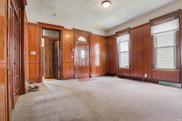 carpeted spare room featuring wooden walls and a textured ceiling