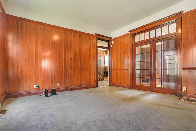 carpeted spare room featuring wooden walls and french doors