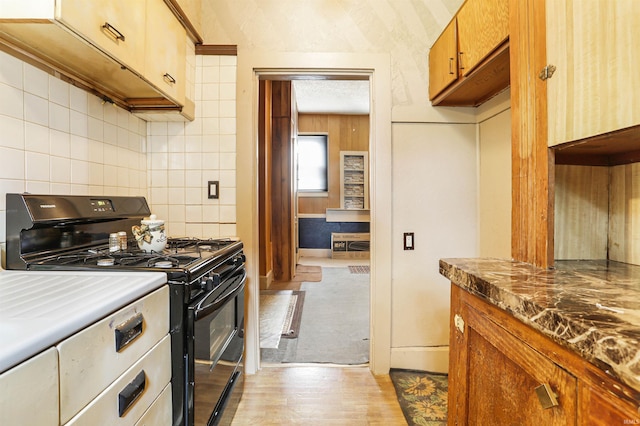 kitchen with brown cabinetry, light wood-style flooring, black range with gas cooktop, and tasteful backsplash