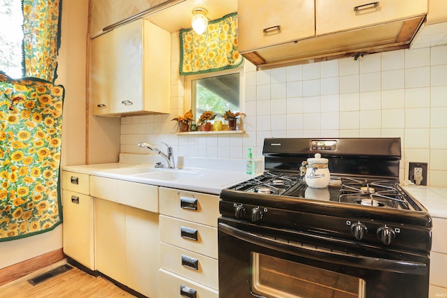 kitchen with visible vents, under cabinet range hood, a sink, tasteful backsplash, and black range with gas cooktop