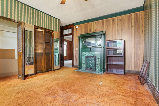 unfurnished living room with wallpapered walls, a fireplace with flush hearth, carpet floors, a textured ceiling, and a ceiling fan