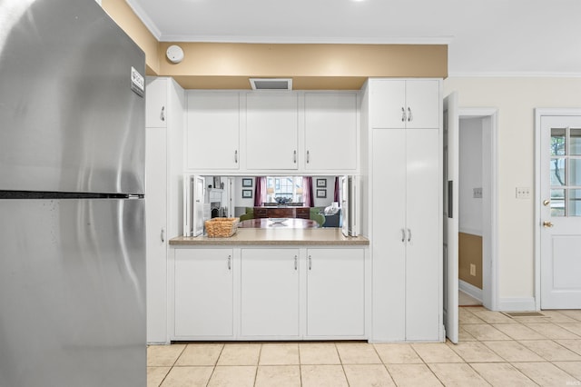 kitchen with light tile patterned floors, ornamental molding, stainless steel fridge, and white cabinetry