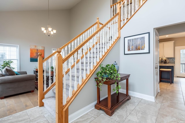 stairway featuring baseboards, a high ceiling, and a chandelier