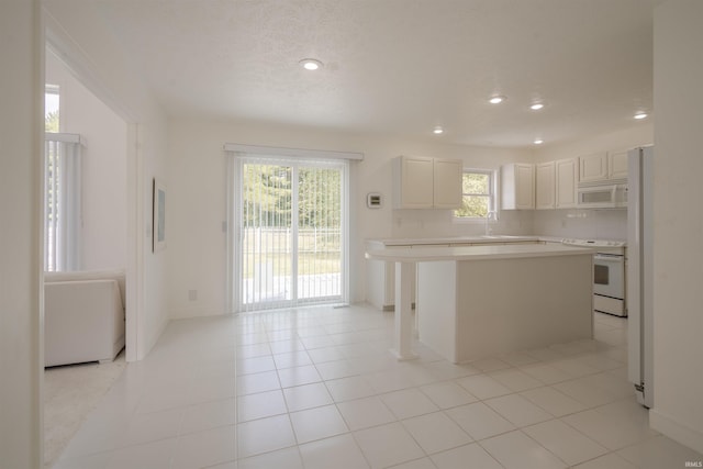 kitchen featuring light countertops, a kitchen island, light tile patterned floors, and white appliances