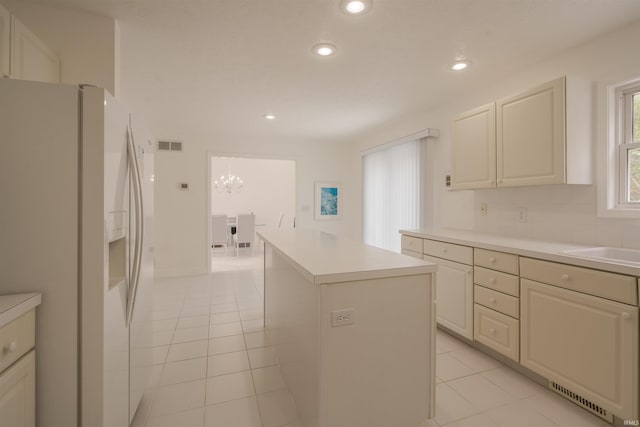 kitchen featuring light countertops, a kitchen island, white refrigerator with ice dispenser, light tile patterned floors, and decorative backsplash