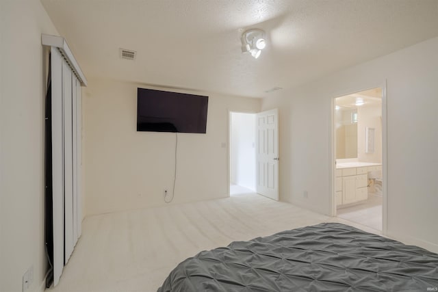 carpeted bedroom with visible vents, ensuite bathroom, and a textured ceiling