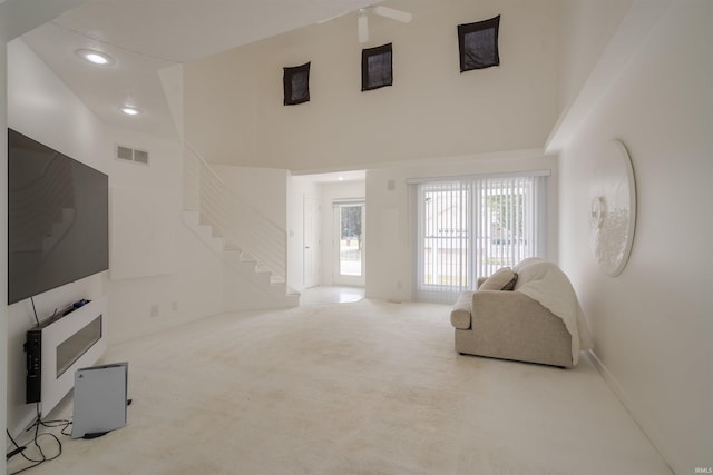 living room with ceiling fan, carpet floors, and a high ceiling