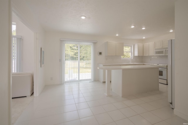 kitchen with white appliances, light tile patterned floors, a center island, and plenty of natural light