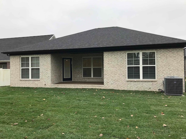 back of property featuring a shingled roof, central AC, a yard, and brick siding