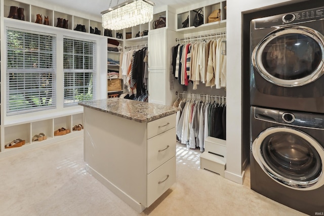 laundry area featuring stacked washer and clothes dryer, an inviting chandelier, and light colored carpet