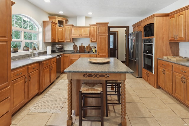 kitchen with a kitchen bar, a center island, stainless steel appliances, sink, and light tile patterned flooring