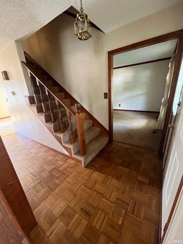 stairway with a textured ceiling, a chandelier, and parquet floors