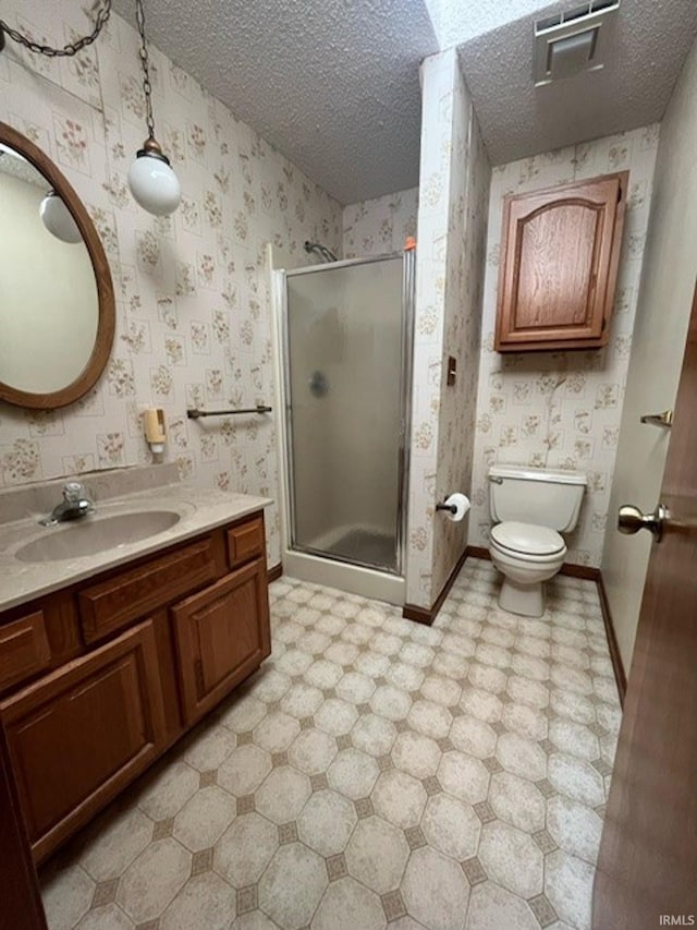 bathroom with vanity, toilet, a shower with shower door, and a textured ceiling