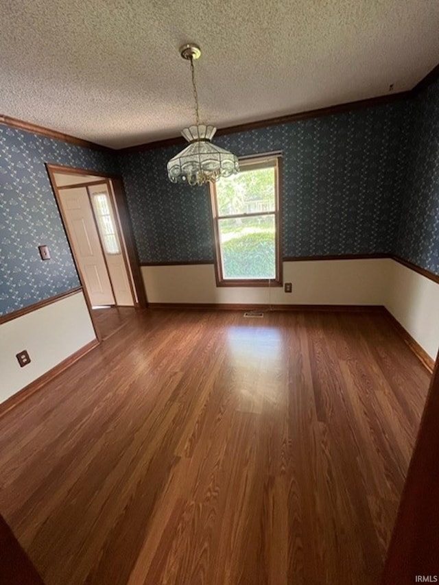 empty room with hardwood / wood-style flooring, ornamental molding, an inviting chandelier, and a textured ceiling