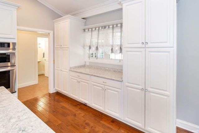 kitchen with crown molding, stainless steel double oven, white cabinetry, and hardwood / wood-style floors