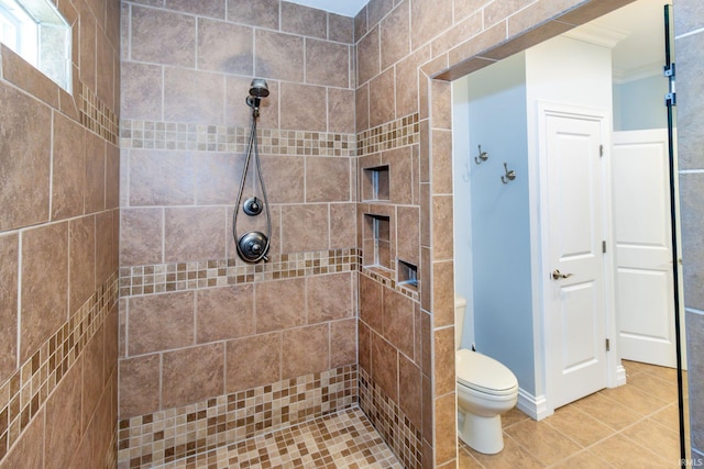 bathroom with tile patterned floors, toilet, a tile shower, and ornamental molding