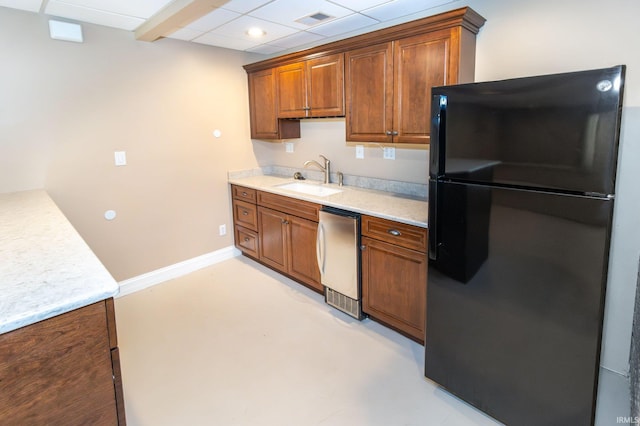 kitchen with stainless steel refrigerator, sink, light stone countertops, and black fridge