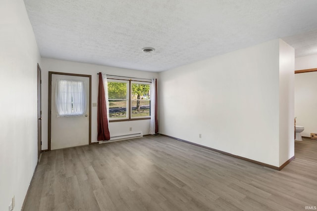 empty room featuring a textured ceiling, baseboard heating, and light hardwood / wood-style floors