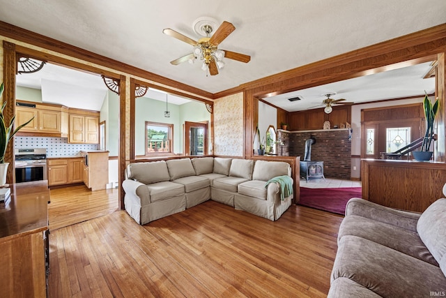 living room featuring light wood-type flooring, ceiling fan, a wood stove, and crown molding