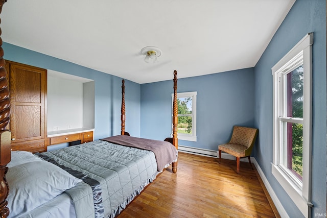 bedroom with multiple windows, baseboard heating, and light hardwood / wood-style floors