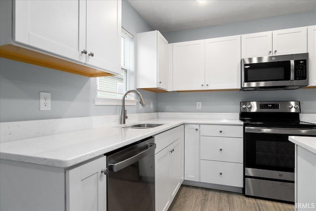 kitchen featuring light wood-type flooring, light stone counters, sink, appliances with stainless steel finishes, and white cabinets