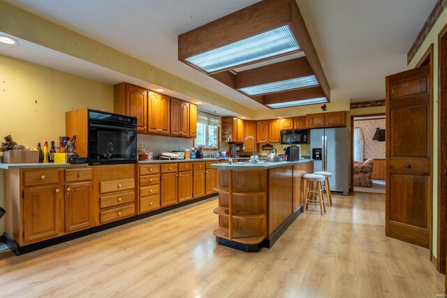 kitchen with light wood-type flooring, black appliances, an island with sink, and a breakfast bar