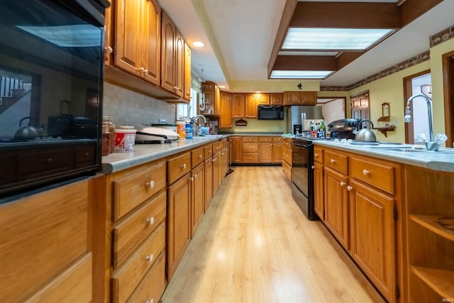 kitchen featuring black appliances, backsplash, sink, and light hardwood / wood-style floors