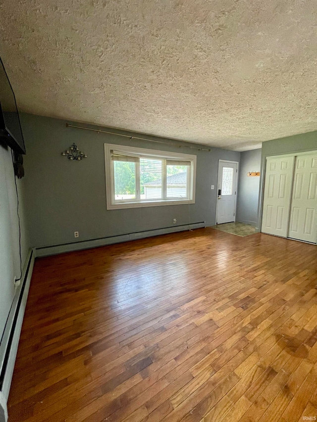 unfurnished living room featuring baseboard heating, a textured ceiling, and wood-type flooring