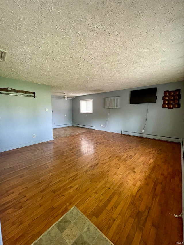 unfurnished living room with hardwood / wood-style floors, a wall unit AC, baseboard heating, and a textured ceiling