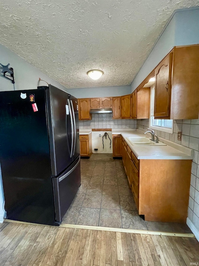 kitchen with a textured ceiling, tasteful backsplash, sink, black refrigerator, and light wood-type flooring