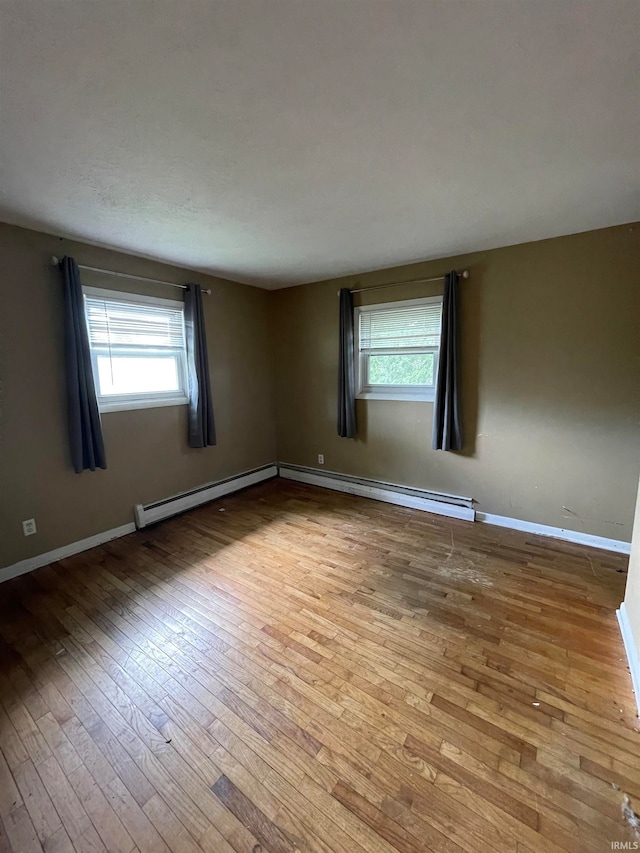 spare room featuring a baseboard heating unit, a healthy amount of sunlight, and light wood-type flooring