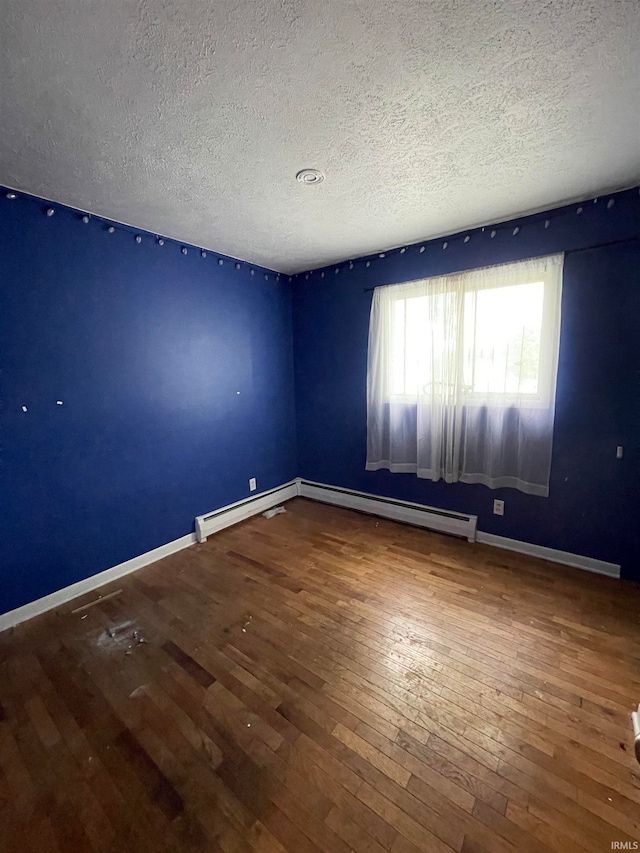 empty room with wood-type flooring, a baseboard radiator, and a textured ceiling