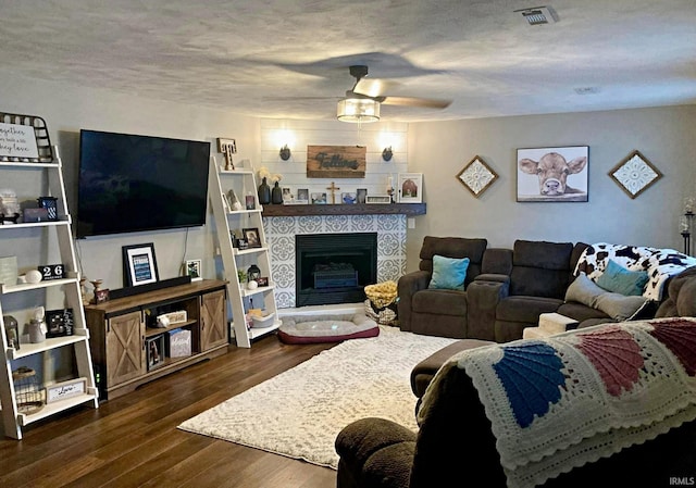 living room with a textured ceiling, a tile fireplace, ceiling fan, and dark hardwood / wood-style floors