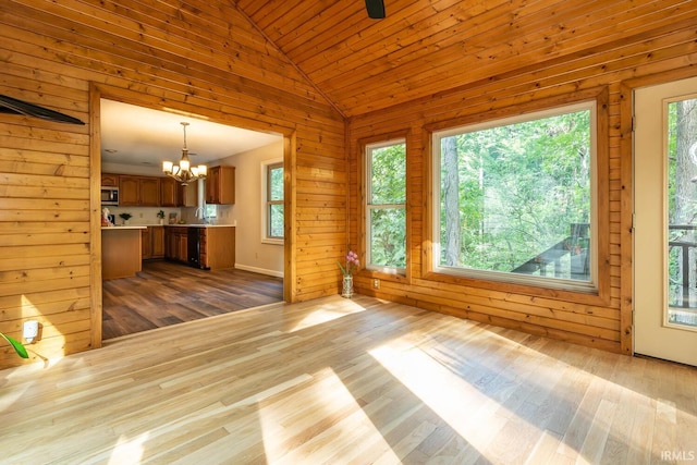 unfurnished living room featuring wooden walls, hardwood / wood-style flooring, a notable chandelier, and a healthy amount of sunlight