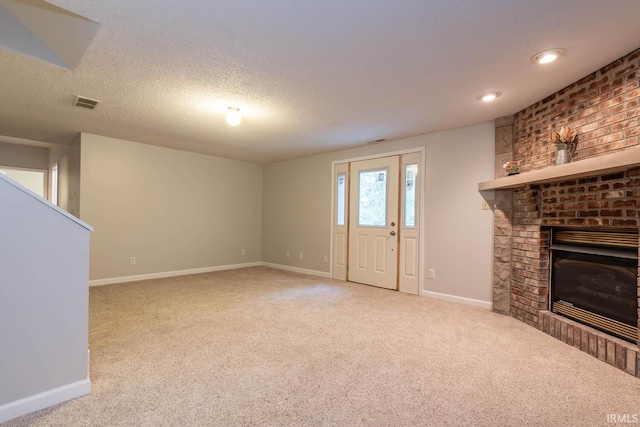 unfurnished living room with a textured ceiling, light colored carpet, and a brick fireplace