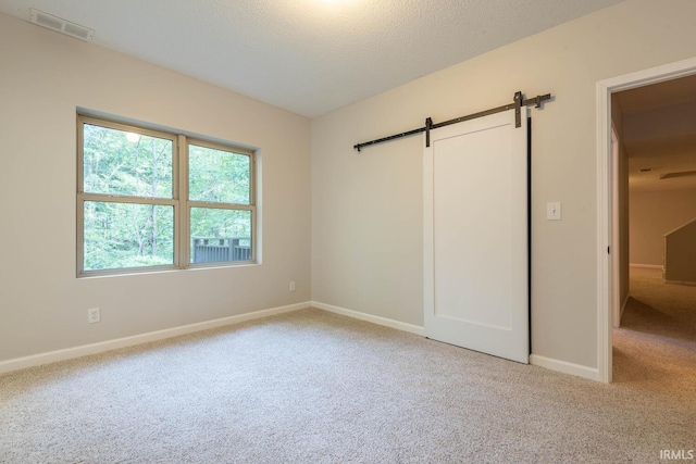 unfurnished bedroom featuring a barn door, light colored carpet, and a textured ceiling