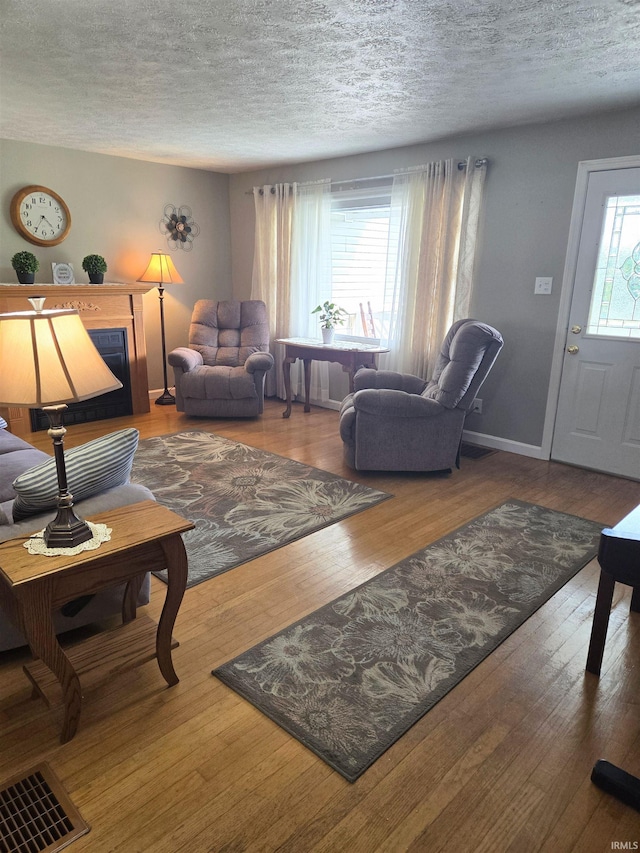 living room with visible vents, a textured ceiling, baseboards, and wood finished floors