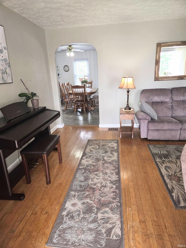 living room with a textured ceiling, wood-type flooring, ceiling fan, and a wealth of natural light