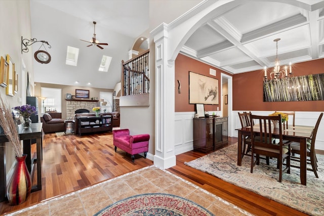 dining area featuring a fireplace, coffered ceiling, ceiling fan with notable chandelier, wood-type flooring, and beam ceiling